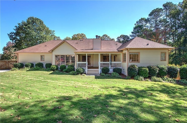 view of front facade with covered porch, a front lawn, a chimney, and fence