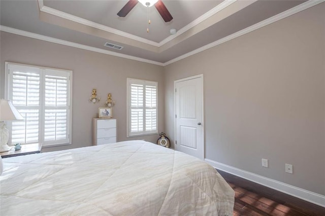 bedroom with dark wood-type flooring, ceiling fan, ornamental molding, and a tray ceiling