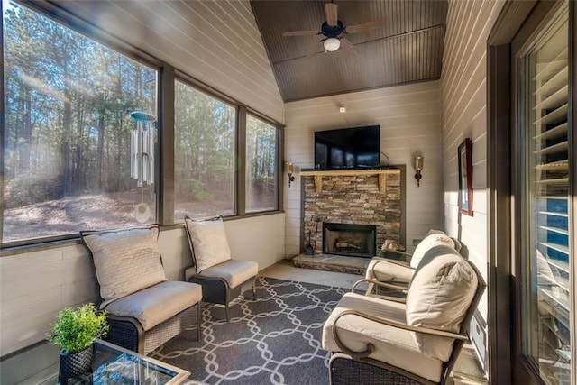 sunroom featuring ceiling fan, lofted ceiling, and a stone fireplace