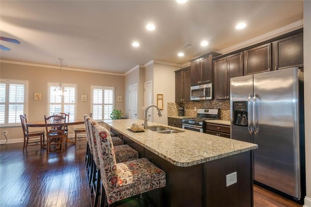 kitchen with appliances with stainless steel finishes, pendant lighting, an island with sink, sink, and dark brown cabinetry