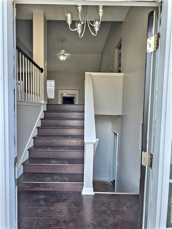 stairs with ceiling fan with notable chandelier and wood finished floors