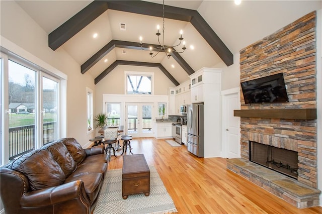 living room featuring a notable chandelier, a stone fireplace, a wealth of natural light, and high vaulted ceiling