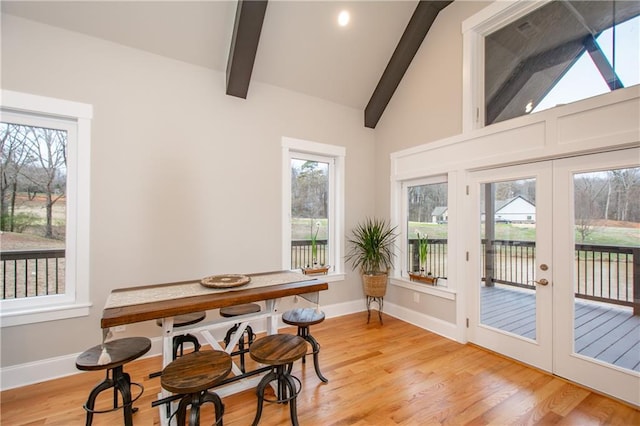 dining room with lofted ceiling with beams, a healthy amount of sunlight, light wood-type flooring, and french doors