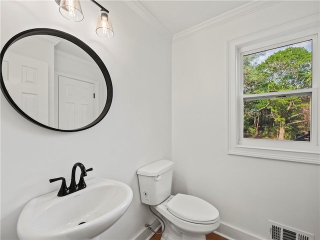 bathroom with baseboards, crown molding, toilet, visible vents, and a sink