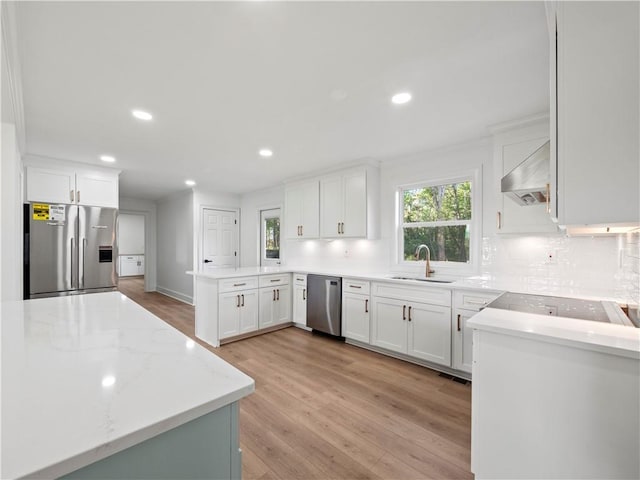 kitchen featuring a peninsula, ventilation hood, appliances with stainless steel finishes, a sink, and decorative backsplash