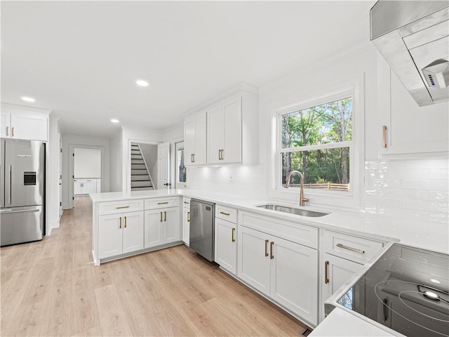 kitchen with white cabinets, wall chimney exhaust hood, a sink, appliances with stainless steel finishes, and a peninsula