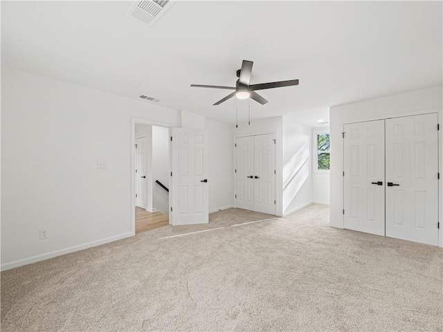 unfurnished bedroom with two closets, visible vents, baseboards, and light colored carpet