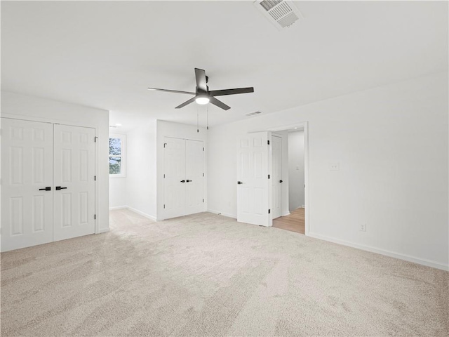 unfurnished bedroom with light colored carpet, a ceiling fan, visible vents, multiple closets, and baseboards