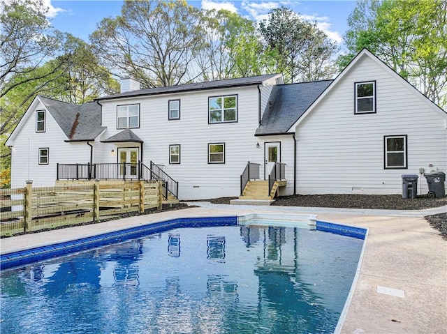 back of house with a chimney, fence, a wooden deck, a fenced in pool, and roof with shingles