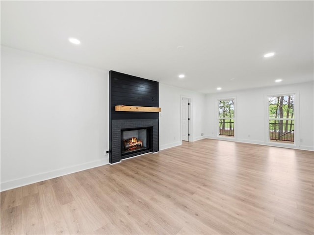 unfurnished living room featuring recessed lighting, a fireplace, light wood finished floors, and baseboards