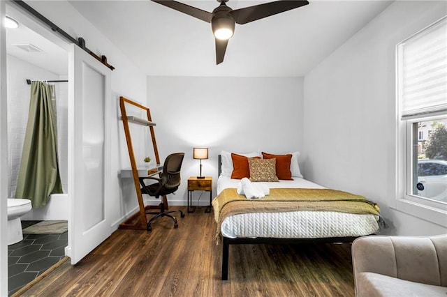bedroom featuring visible vents, connected bathroom, a barn door, and wood finished floors