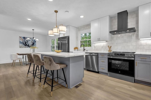 kitchen with a kitchen breakfast bar, gray cabinets, a center island, wall chimney exhaust hood, and appliances with stainless steel finishes