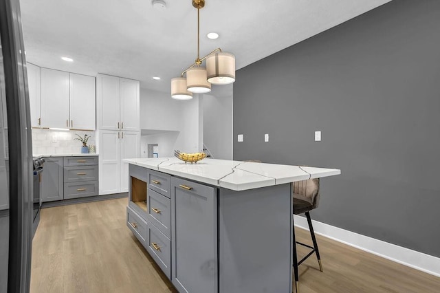 kitchen with a breakfast bar, gray cabinets, light wood-style flooring, and a kitchen island