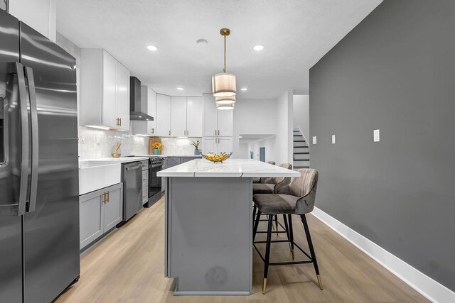 kitchen featuring decorative backsplash, stainless steel appliances, a kitchen island, wall chimney exhaust hood, and a kitchen breakfast bar