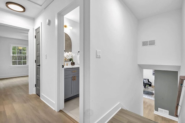 hallway featuring baseboards, visible vents, and light wood finished floors