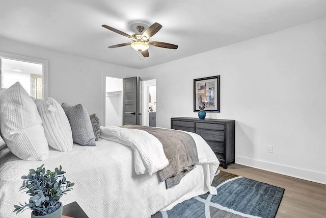 bedroom featuring a closet, ceiling fan, baseboards, wood finished floors, and a spacious closet