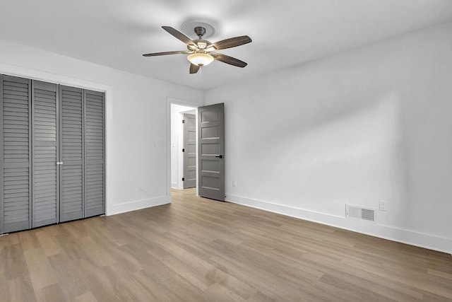 unfurnished bedroom with wood finished floors, visible vents, a closet, and baseboards