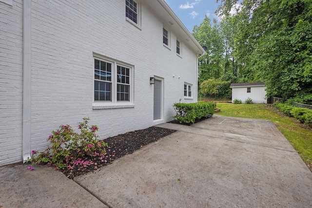 view of home's exterior with a patio area, a yard, brick siding, and an outbuilding