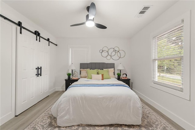 bedroom featuring ceiling fan, a barn door, and light hardwood / wood-style flooring