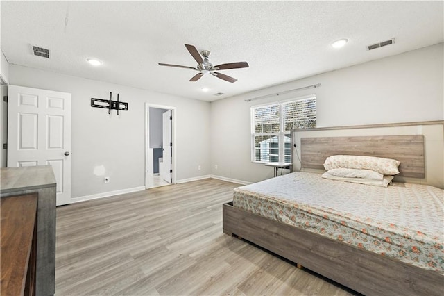 bedroom with a textured ceiling, wood finished floors, visible vents, and baseboards