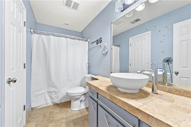 bathroom with stone finish flooring, visible vents, vanity, and toilet