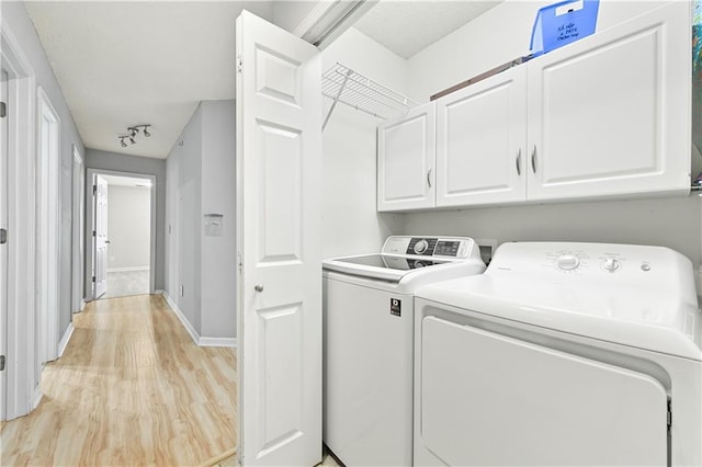 clothes washing area with light wood-type flooring, washing machine and dryer, cabinet space, and baseboards