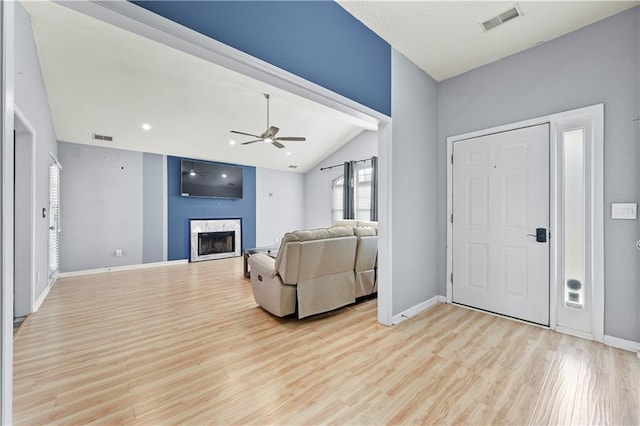 living room featuring vaulted ceiling, light wood-style flooring, a fireplace, and visible vents