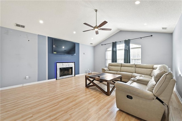 living room with a fireplace, lofted ceiling, light wood-style floors, a ceiling fan, and a textured ceiling