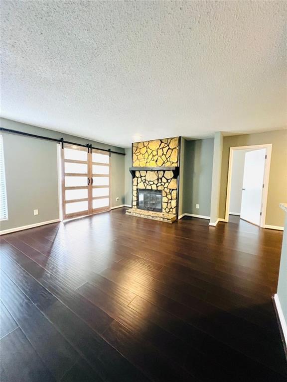 unfurnished living room with a textured ceiling, baseboards, wood finished floors, a stone fireplace, and a barn door