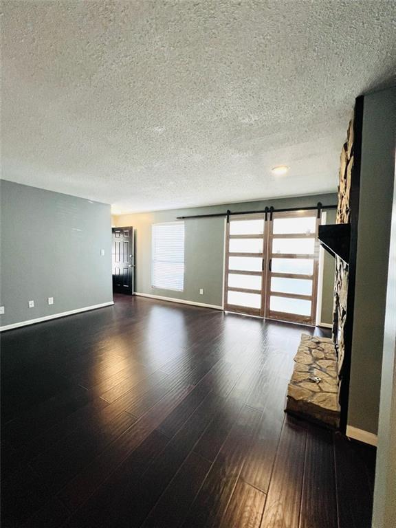 unfurnished living room featuring dark wood-style floors, a barn door, a textured ceiling, and baseboards