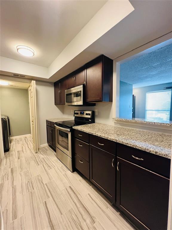kitchen with light wood-style flooring, baseboards, stainless steel appliances, dark brown cabinetry, and light stone counters