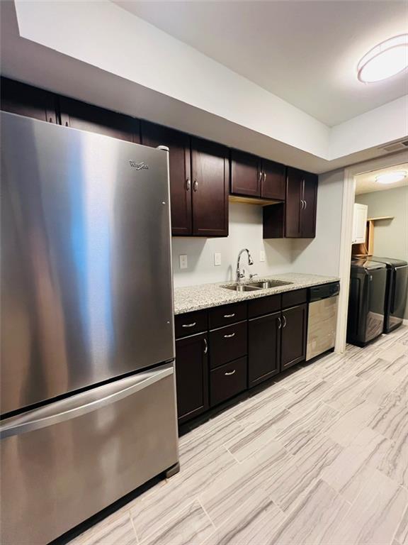 kitchen featuring independent washer and dryer, stainless steel appliances, dark brown cabinets, a sink, and light stone counters