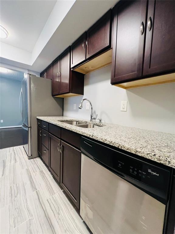 kitchen with a sink, light stone countertops, appliances with stainless steel finishes, and dark brown cabinets