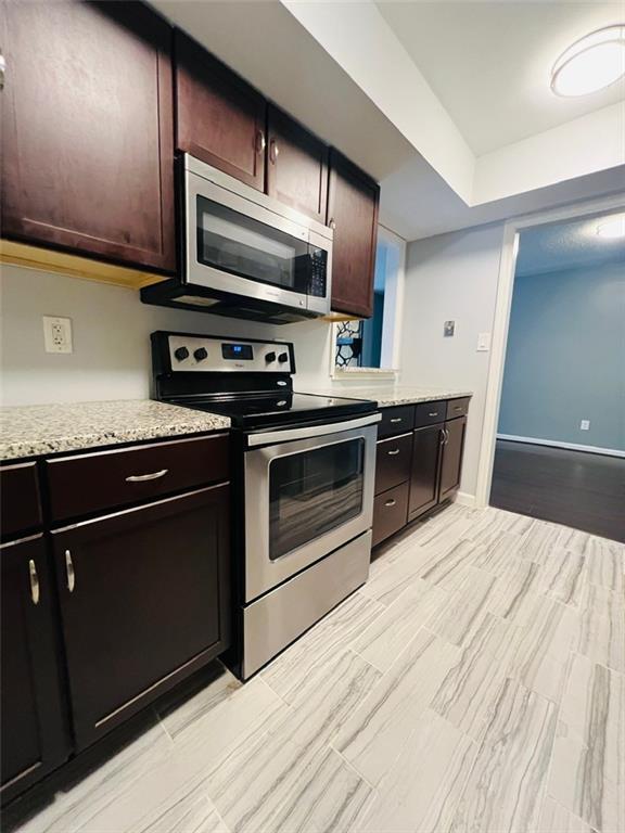 kitchen featuring light stone countertops, dark brown cabinets, appliances with stainless steel finishes, and baseboards