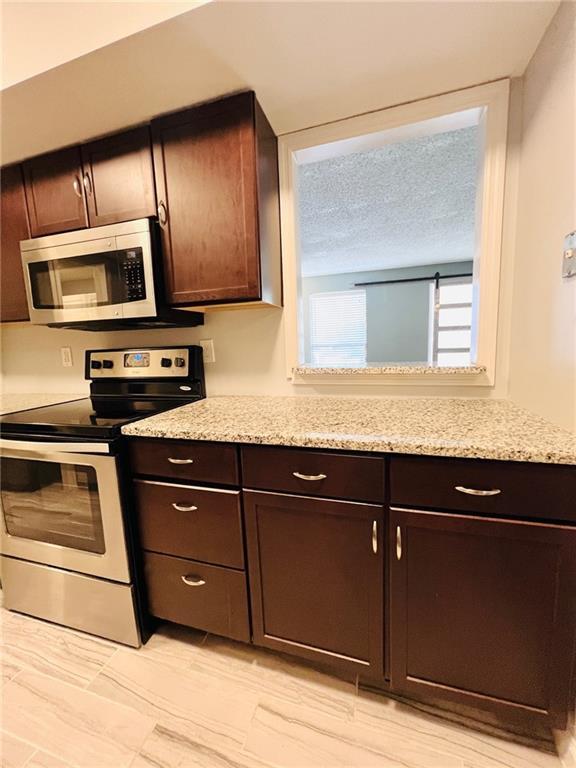 kitchen with light stone countertops, dark brown cabinetry, appliances with stainless steel finishes, and a textured ceiling