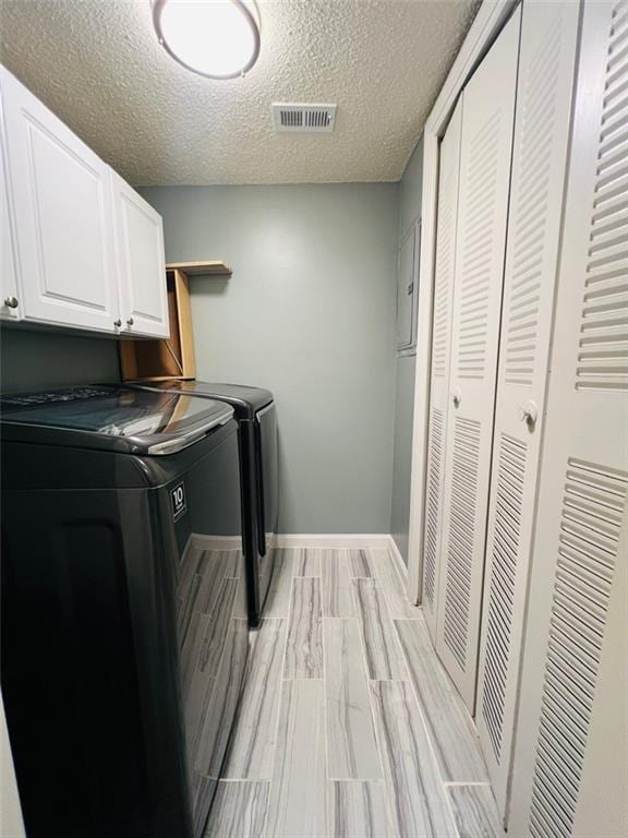 washroom featuring separate washer and dryer, a textured ceiling, baseboards, visible vents, and cabinet space