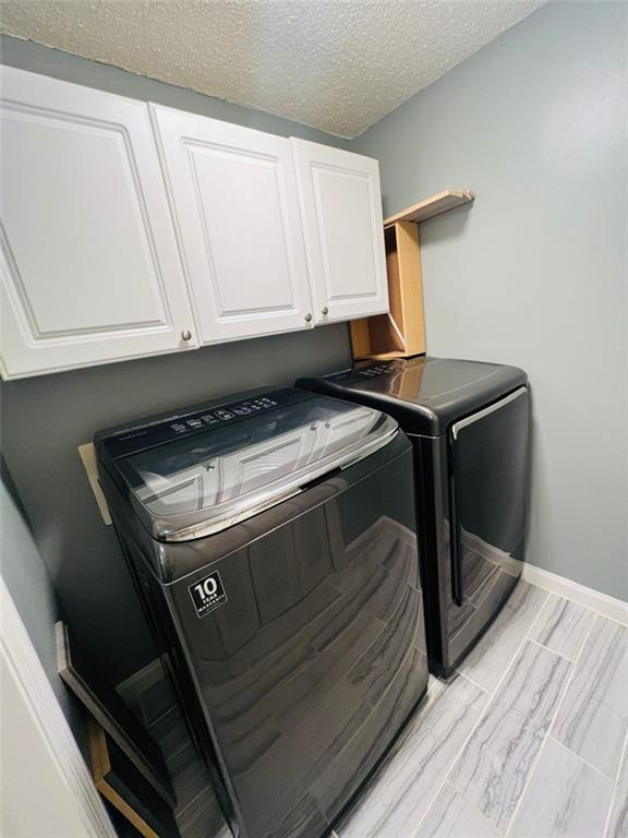 washroom with cabinet space, baseboards, washer and dryer, and a textured ceiling