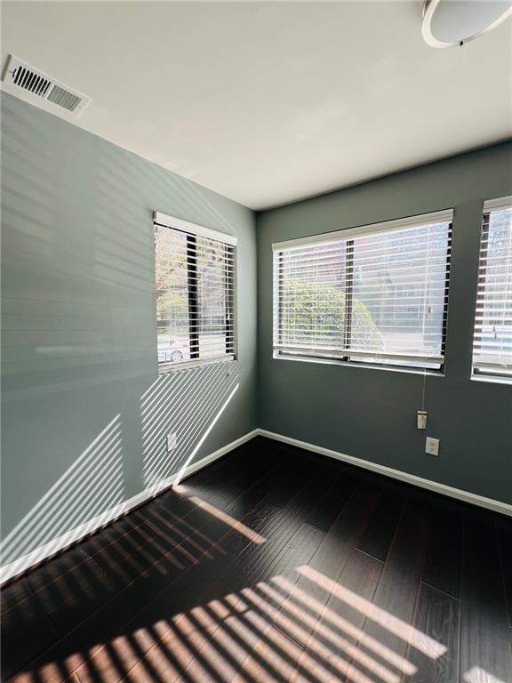 unfurnished room featuring baseboards, visible vents, plenty of natural light, and wood finished floors