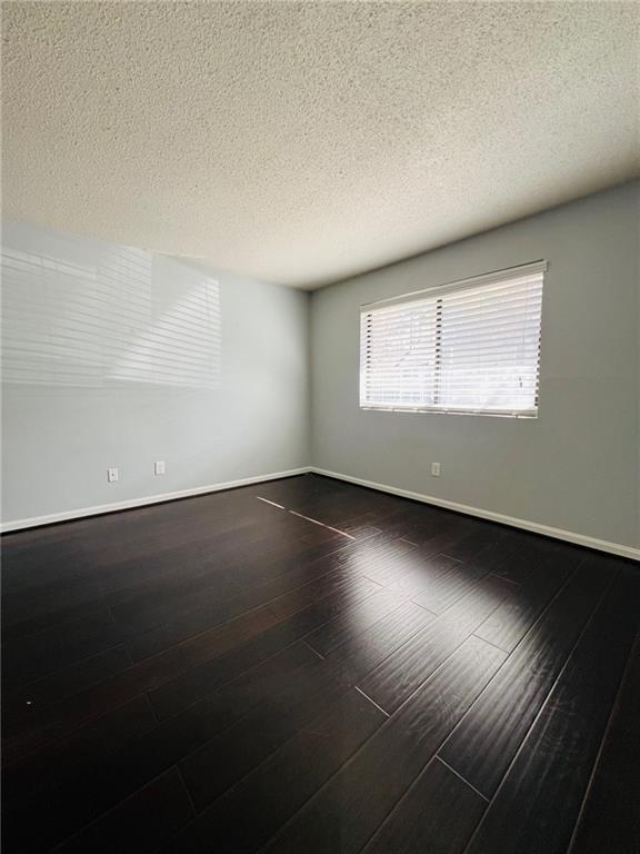 unfurnished room with baseboards, a textured ceiling, and dark wood-style floors