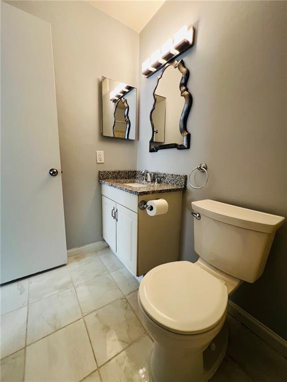 half bath with baseboards, toilet, and vanity