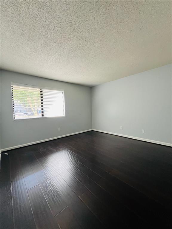 spare room with baseboards, dark wood-type flooring, and a textured ceiling