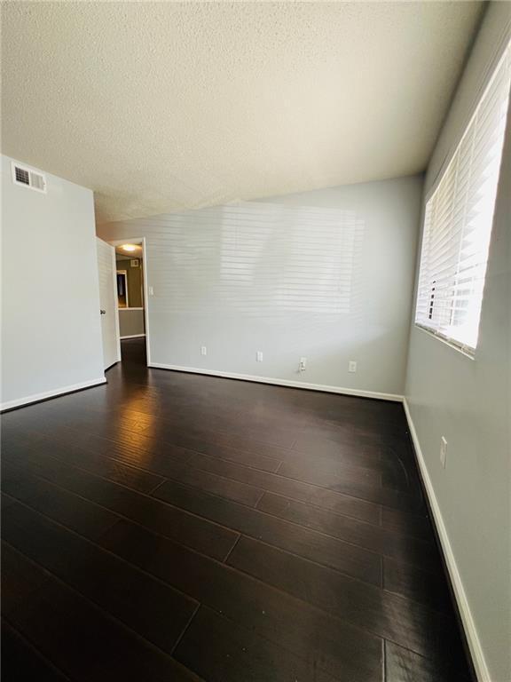 spare room featuring a textured ceiling, baseboards, dark wood-type flooring, and visible vents
