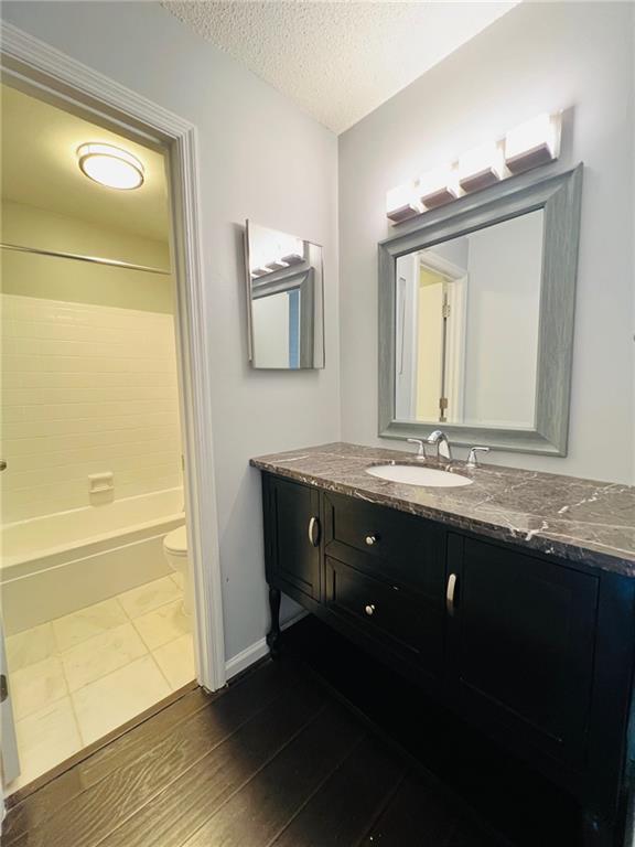 bathroom with vanity, toilet, a textured ceiling, shower / bathtub combination, and wood finished floors