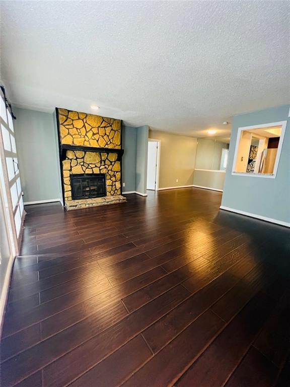 unfurnished living room with a stone fireplace, a textured ceiling, baseboards, and wood finished floors