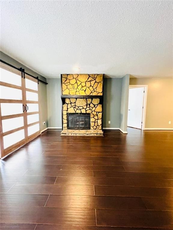 unfurnished living room with a stone fireplace, a barn door, wood finished floors, and a textured ceiling