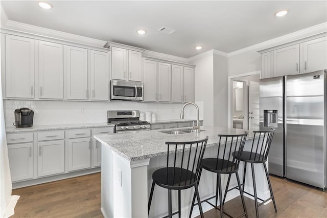 kitchen with stainless steel appliances, visible vents, a sink, and an island with sink