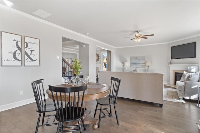 dining room featuring dark wood-style floors, stairway, ornamental molding, and a glass covered fireplace