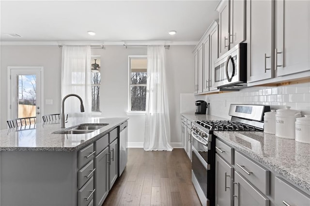 kitchen with crown molding, a center island with sink, stainless steel appliances, gray cabinetry, and a sink