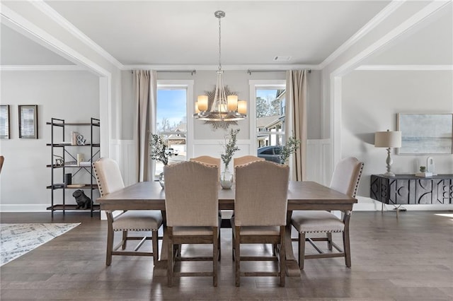 dining area with crown molding, dark wood-type flooring, a notable chandelier, and wainscoting