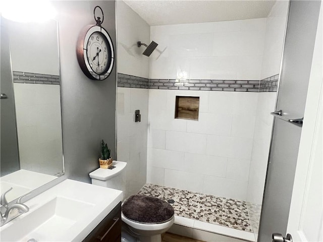 bathroom with tiled shower, a textured ceiling, vanity, and toilet